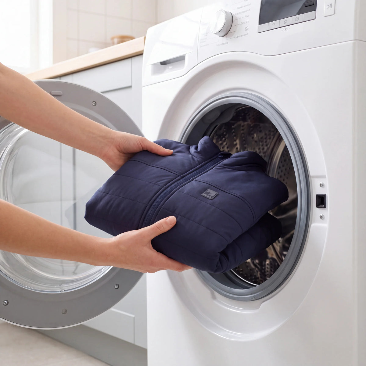 Hands placing a folded Sagney heated puffer jacket into a front-loading washing machine